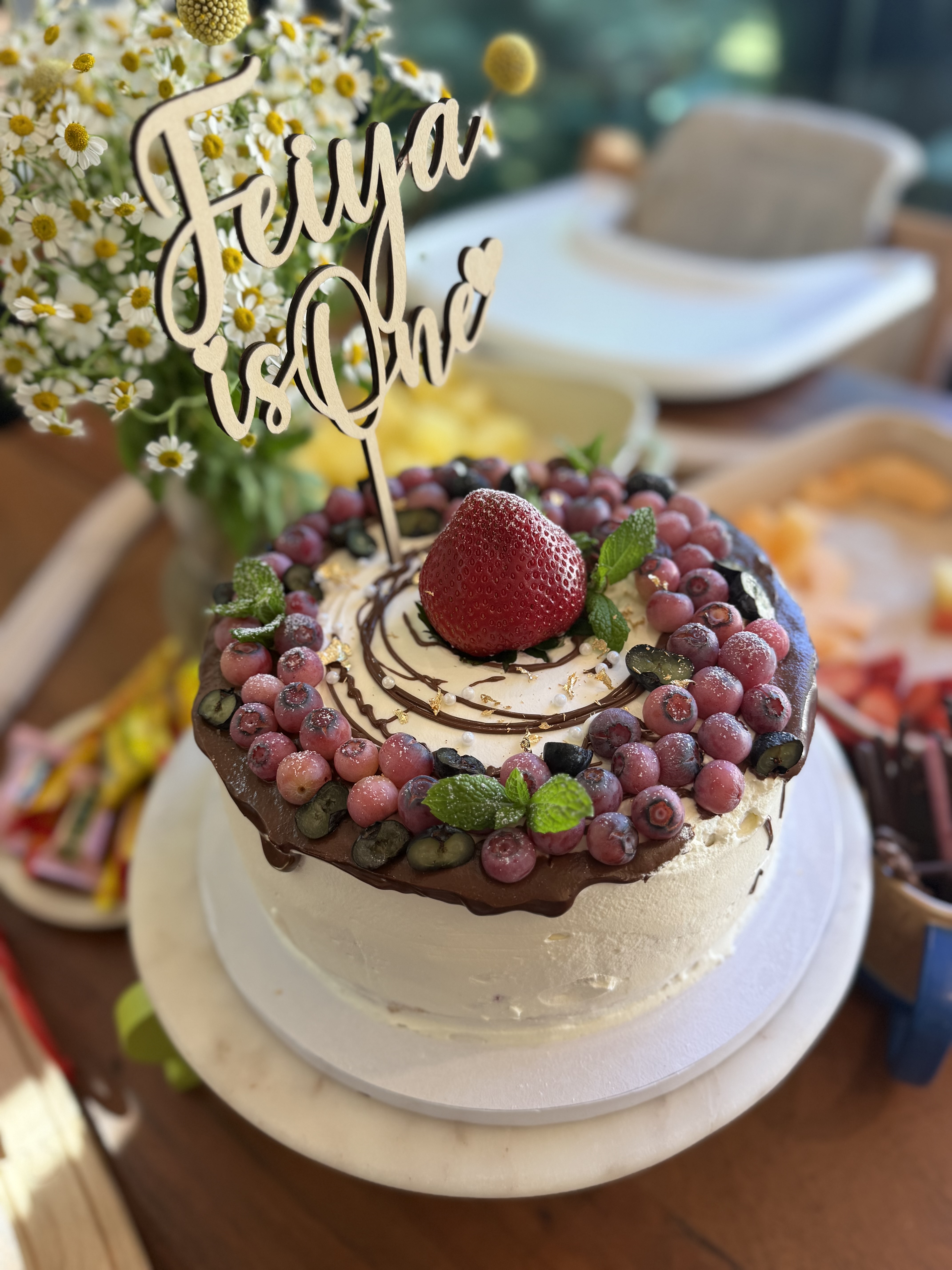First-birthday cake with fresh berries and a custom topper